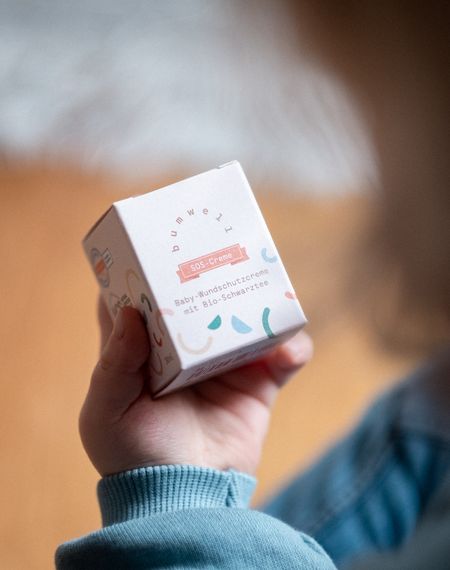 Kind hält bumwell Baby-Wundschutzcreme SOS-Creme in den Händen - Bio-Naturkosmetik mit Schwarztee