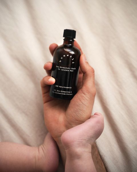 bumwell Baby-Wundschutz Liquid in Frauenhand mit Babyfüßen