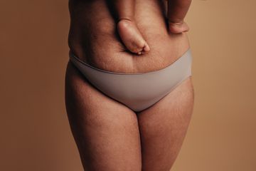 Frau mit postnatalem Bauch und Baby auf dem Arm